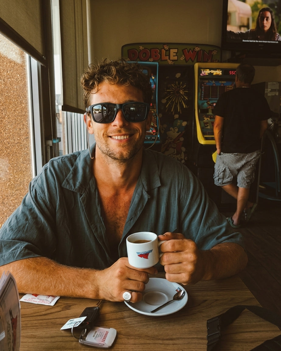 Smiling man wearing Ocean sunglasses with a coffee at a beach bar